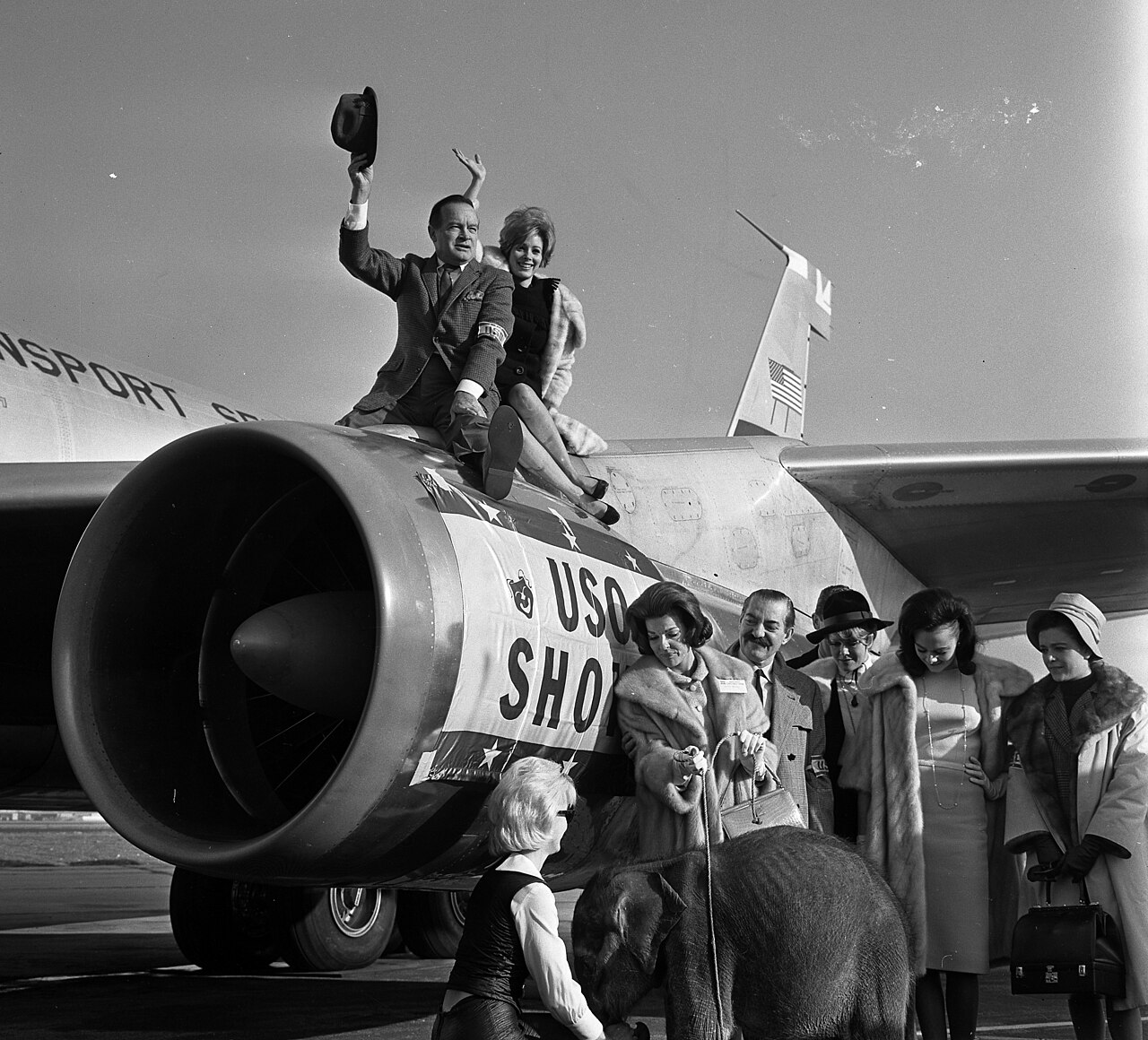 Bob Hope and actress Jill St. John perch on jet engine before taking off from Los Angeles International Airport on a flight to Southeast Asia for the 13th annua (1964)