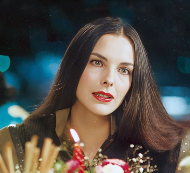 Carole Bouquet à table sur la terrasse d'un restaurant, la nuit, lors des fêtes de fin d'années. Elle porte ses cheveux longs noirs et lisses avec la raie au mi (1982)