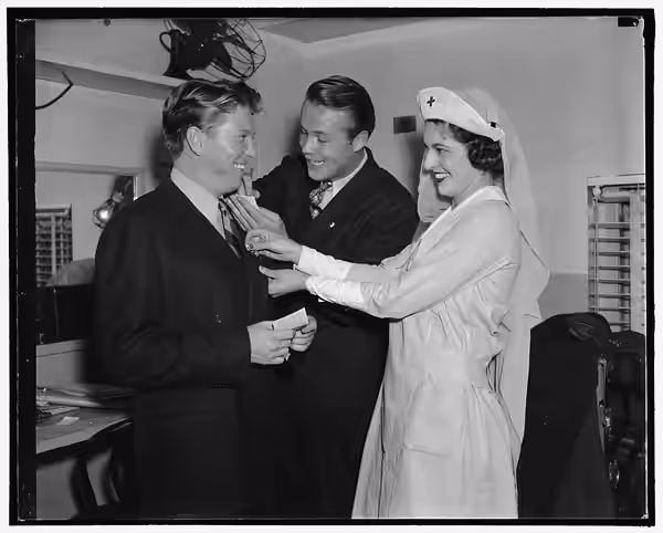 Title: Picture stars enroll in Red Cross. Between appearances at the Earle Theater Johnny Davis, (left) and Wayne Morris receive their Red Cross pins from Miss  (1938)