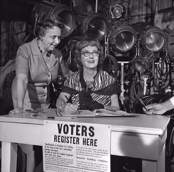SIGNS UP—Bette Davis, at work on 20th Century Fox movie, is registered to vote by a deputy registrar, Mrs. Irma Green, who visited the set. (1964)