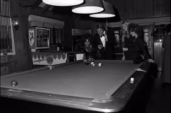 Ryan O'Neal, surrounded by Playboy bunnies, tries out the pool table in the playhouse of Hugh Hefner's Playboy Mansion West in Holmby Hills. (1971)