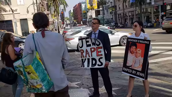 Patrick Little and a woman standing on one of the sidewalks of Hollywood Boulevard, Los Angeles holding hateful placards. Bystanders denounce them. (2018)