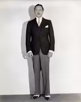 Omschrijving: Kledingstukken: Acteur Edmund Lowe draagt een kostuum met pochet en slobkousen over zijn schoenen, circa 1930.