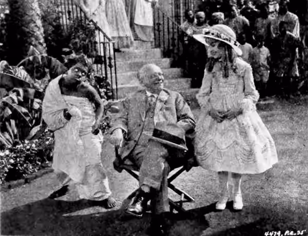 Still from the American drama film Uncle Tom's Cabin (1927) with Mona Ray as Topsy, producer Carl Laemmle, and Virginia Grey as Eva, on page 11 of the March 19,