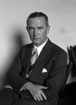 Hollywood film producer John W. Considine, Jr. poses for a photograph, seated with his arms folded. (1920)