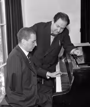 Paul Wittgenstein plays piano with left hand for composer Erich Wolfgang Korngold in Los Angeles. This photograph may be associated with the article, “WITTGENST (1934)