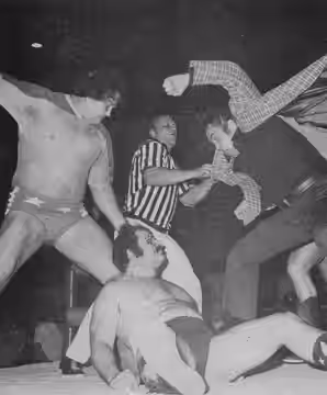 Professional wrestler Bill Watts being attacked by Bob Roop, Gary Hart and J. J. Dillon (the latter mostly obscured in this camera view). The referee is shown t (1975)