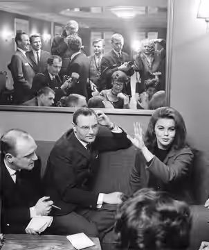 I röd dräkt och svart jumper med helyllestrumpor och svarta stövlar tog Ann-Margret emot pressen. När hennes svenska ordförråd inte förslog tog hon till talande (1963)