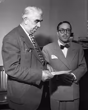 GIVES SELF UP—Dalton Trumbo, film writer, left, pictured with Dep. U.S. Marshal Rossini on surrender in contempt of Congress case. He was released on bond. (1947)