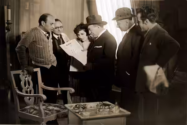 Omschrijving: Speelfilms, regisseurs. Hoofdregisseur Rudolf Meinert van Phönic Film leest samen met een vrouw en omgeven door andere mannen een filmkritiek in e (1928)