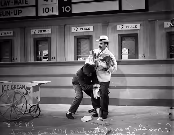 Chico and Groucho Marx standing at ticket windows during filming of scene for A Day at the Races (1937)