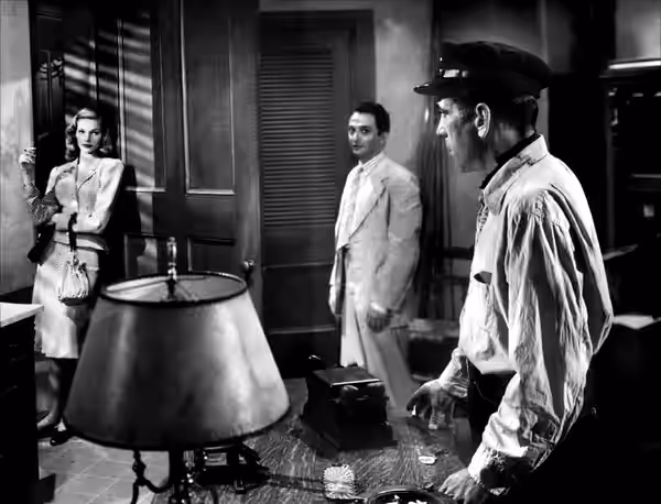 Promotional still from the 1944 film To Have and Have Not. Left to right: Lauren Bacall, Marcel Dalio and Humphrey Bogart. Caption reads as follows: In his room