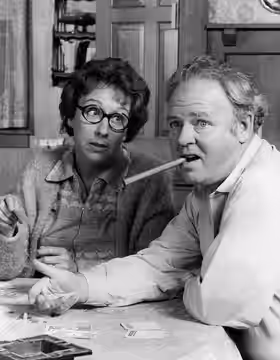 Photo of Jean Stapleton and Carroll O'Connor as Edith and Archie Bunker from the television program All In the Family. During a family Monopoly game, Archie is 