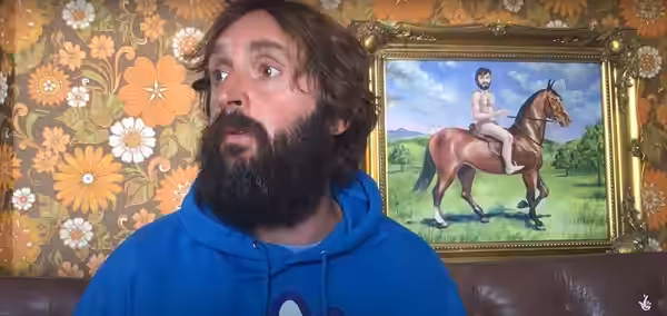 Cropped video still of Joe Wilkinson (left) in front of a painting of a man on a horse (right) in 2020