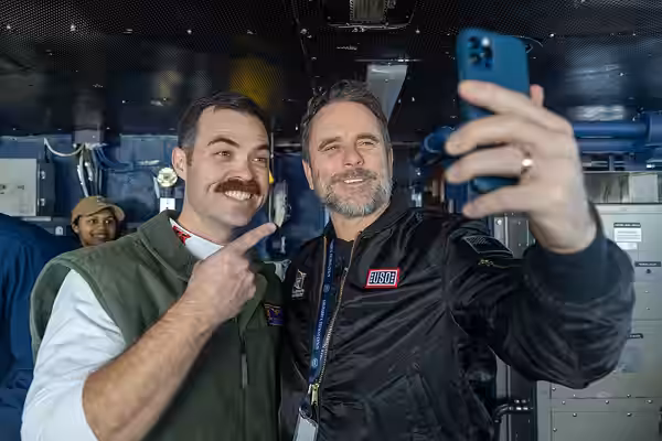 241207-N-SW048-1262 MEDITERRANEAN SEA (Dec. 11, 2024) Charles Esten, right, and Cmdr. John Allen pose for a photo on the bridge aboard the Nimitz-class aircraft