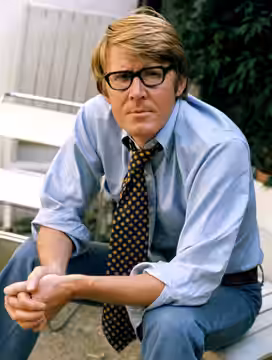 Portrait photograph of Alan Bennett wearing a wide necktie in 1973; taken in photographers garden London