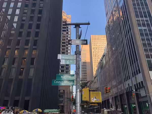 Signs at a street corner in New York City mark Avenue of the Americas, also known as Sixth Avenue. The street additionally has memorial name designations of Pro (2025)
