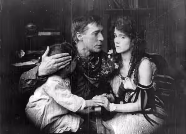 William S. Hart, seated with arms around Margery Wilson and child. Movie still from The Desert Man (1917).