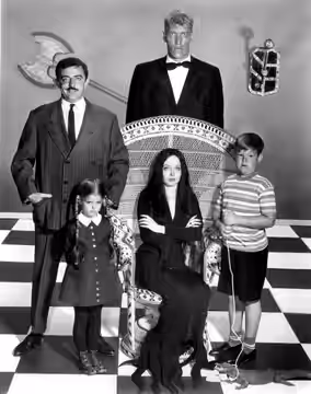 Photo of the main cast of the television program The Addams Family. Standing back from left—John Astin (Gomez), Ted Cassidy (Lurch). Standing, front—Lisa Loring (1964)