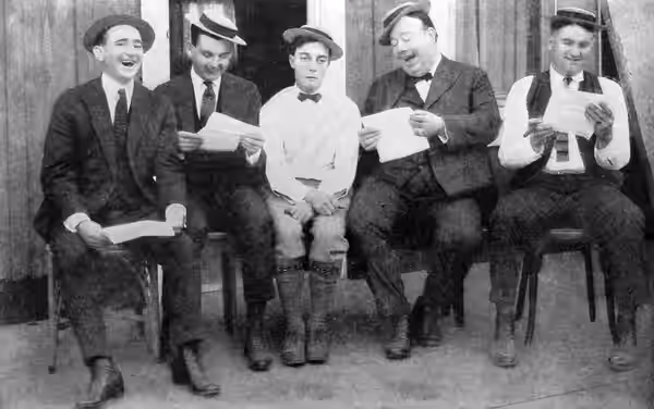 Photograph of Buster Keaton with his writing staff. Caption reads as follows:Buster Keaton's gag department at work, with (left to right) Joe Mitchell, Clyde Br (1923)