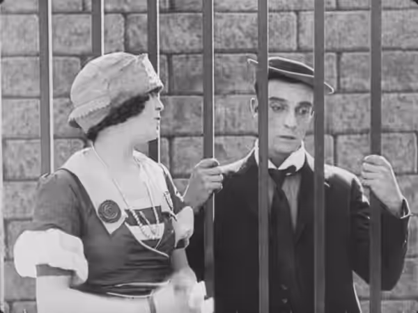 A still from the opening scene of Cops. Keaton's character appears to be in prison, but the next shot shows that he is simply standing behind a gate. (1922)