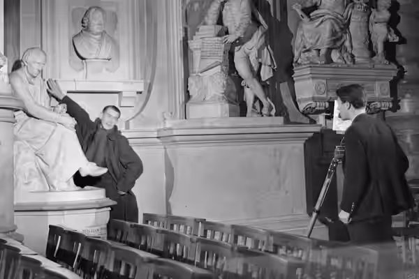 Director Humphrey Jennings stretches to touch a piece of sculpture in Poets' Corner in Westminster Abbey, as he suggests a shot for camera operator Chick Fowle