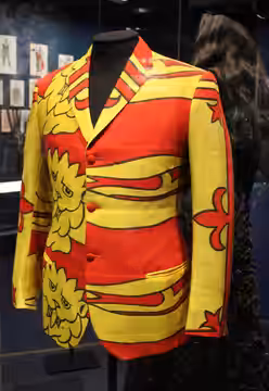 Red and yellow jacket with the Royal Arms of England and Scotland as worn by John Entwistle of The Who about 1966, made by Lew Rose Tailors. Victoria and Albert (2024)