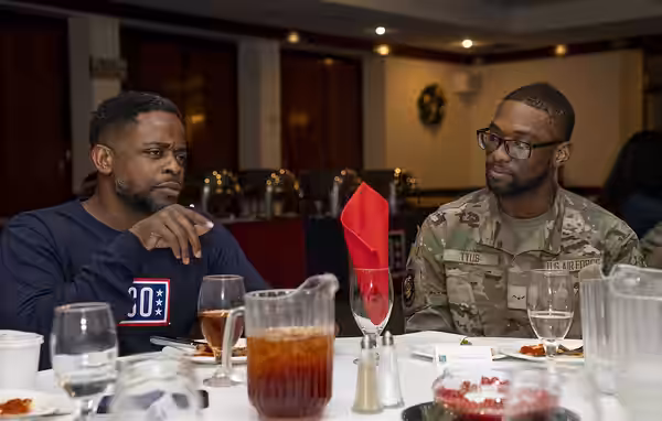 Actor Dulé Hill sits down for a meal with a U.S. Airman during the 2023 USO Holidays Tour at RAF Lakenheath, December 11, 2023. For 82 years, the USO has helped