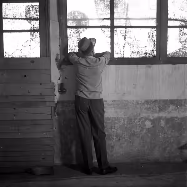 Noé (Haute-Garonne). 9 juillet 1961. Portrait du réalisateur Jacques Tati de dos, accoudé à la fenêtre d'un hangar lors de l'éléction de la "Belle Gaillarde". O