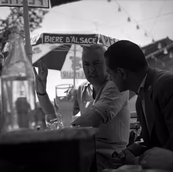 Noé (Haute-Garonne). 9 juillet 1961. Plan rapproché de deux personnes dont le réalisateur Jacques Tati en arrière plan, invité d'honneur de l'éléction de la "Be