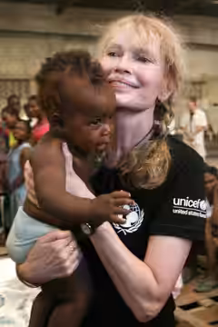 Haiti, September 2008: UNICEF Goodwill Ambassador Mia Farrow holds a baby at a warehouse in the city of Gonaives. The warehouse is sheltering people displaced b