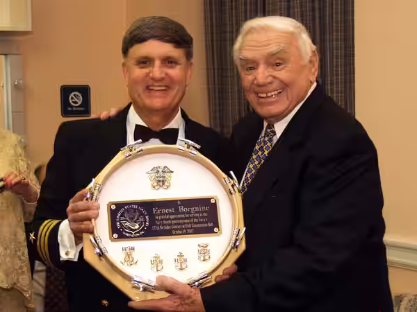 Ernest Borgnine receives a gift. "To Ernest Borgnine in grateful appreciation for serving as the Navy Band's guest narrator of the Navy's 227th Birthday Concert (2002)