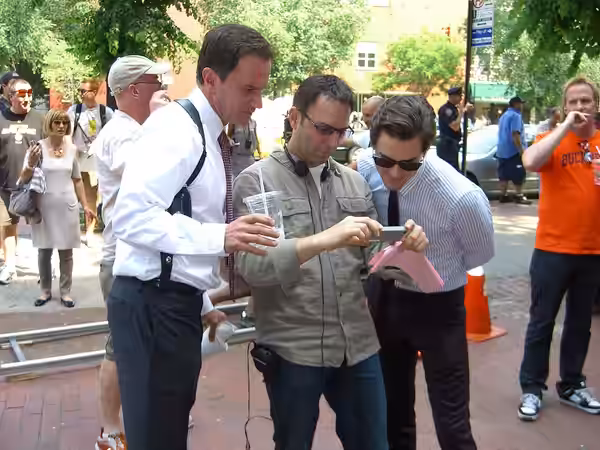 Actors Tim DeKay (left) and Matthew Bomer (right), examining a photograph taken by a production person (center) during the June 7, 2011 production of "On the Fe