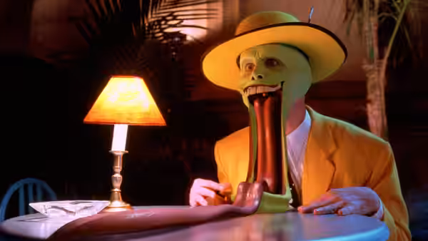 The Mask (Jim Carrey) sits at a table extending his long tongue