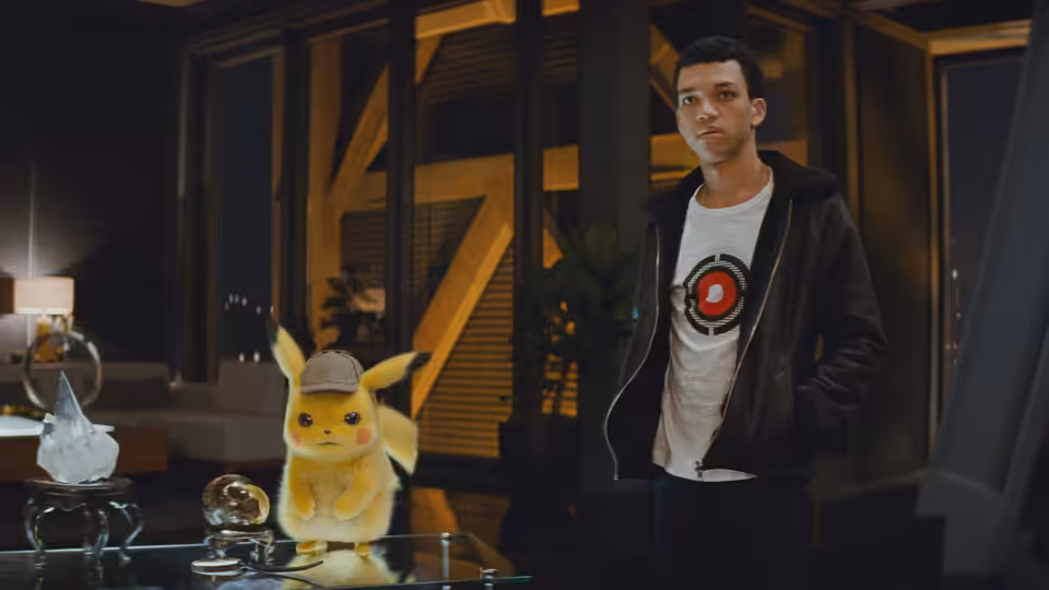 Tim Goodman (Justice Smith) stands beside Detective Pikachu in a modern apartment