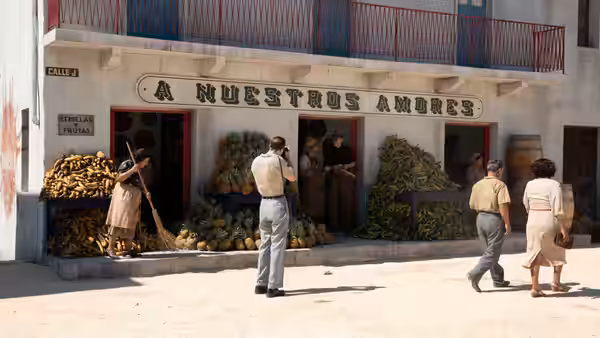 A man talks on the phone outside a fruit market with people nearby