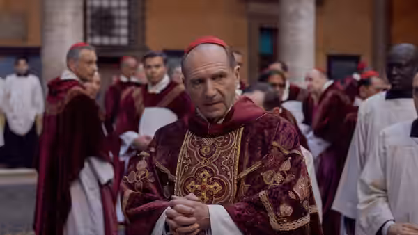 Lawrence (Ralph Fiennes) clasping hands among cardinals in a courtyard
