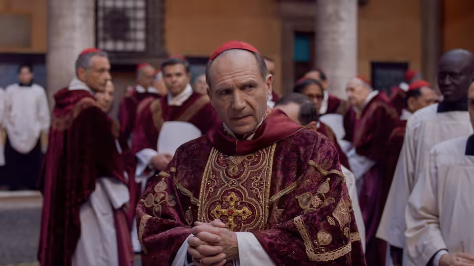 Lawrence (Ralph Fiennes) clasping hands among cardinals in a courtyard