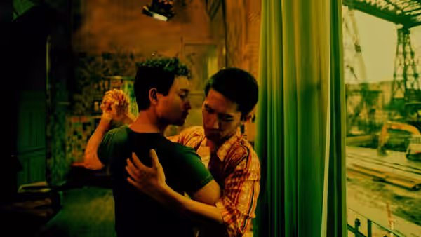 Two men stand close together near a large window