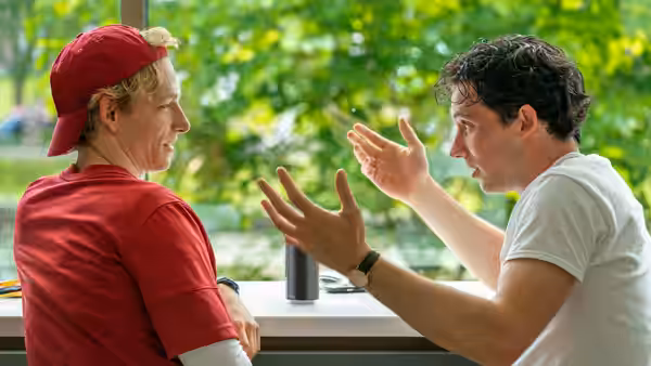 Art (Mike Faist) listening to Patrick (Josh O'Connor) gesturing at a table