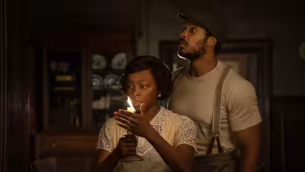 A woman holds a candle while a man stands behind her