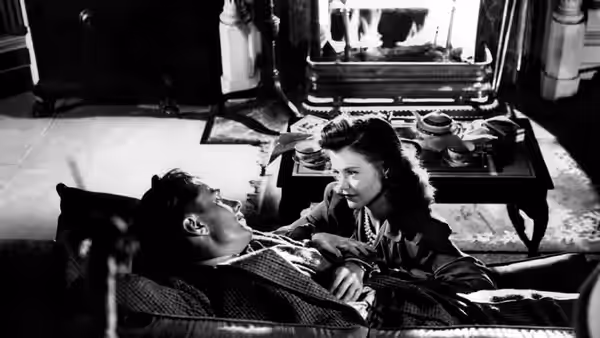 Oliver Reed reclines as Irena Dubrovna leans over him beside a table