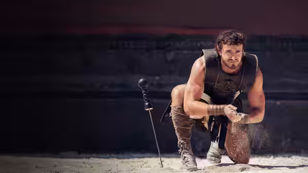 Lucius (Paul Mescal) kneeling in the sand beside a planted sword