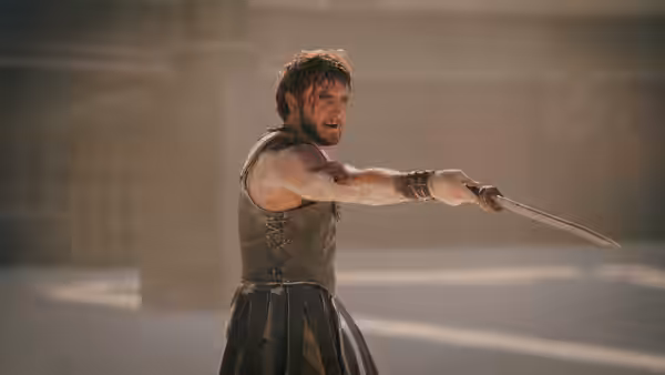 Lucius (Paul Mescal) pointing a sword forward in a dusty arena