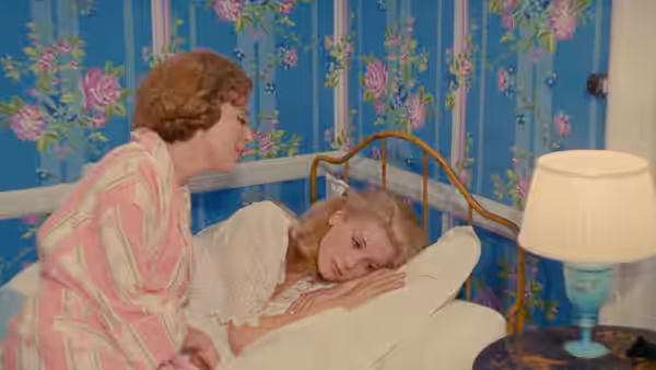 Tante Élise sits beside Geneviève, who lies in bed beneath the covers