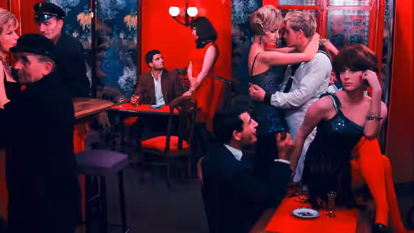 Geneviève and Guy embrace in a restaurant as diners sit at nearby tables