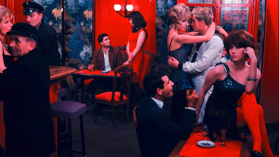 Geneviève and Guy embrace in a restaurant as diners sit at nearby tables
