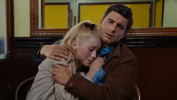Guy comforts Geneviève as she leans against his shoulder indoors