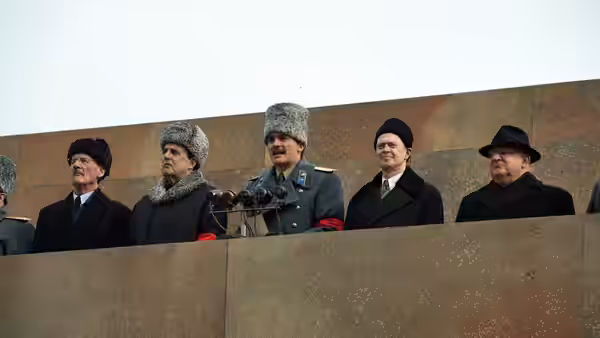 Officials in winter coats and hats stand on a stone balcony