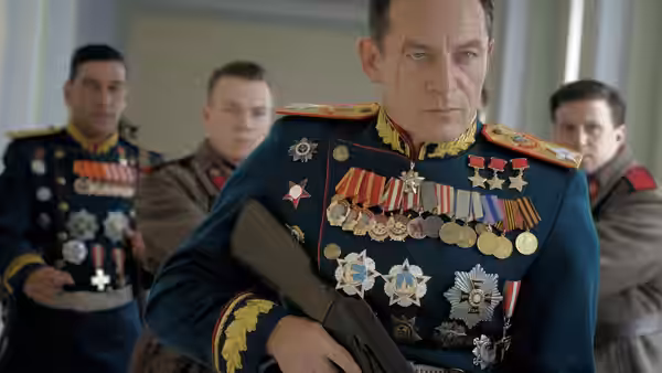 A medal-covered officer in uniform stands with soldiers in the background